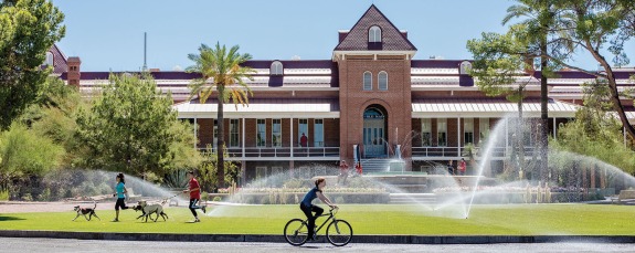 student riding bike past old main